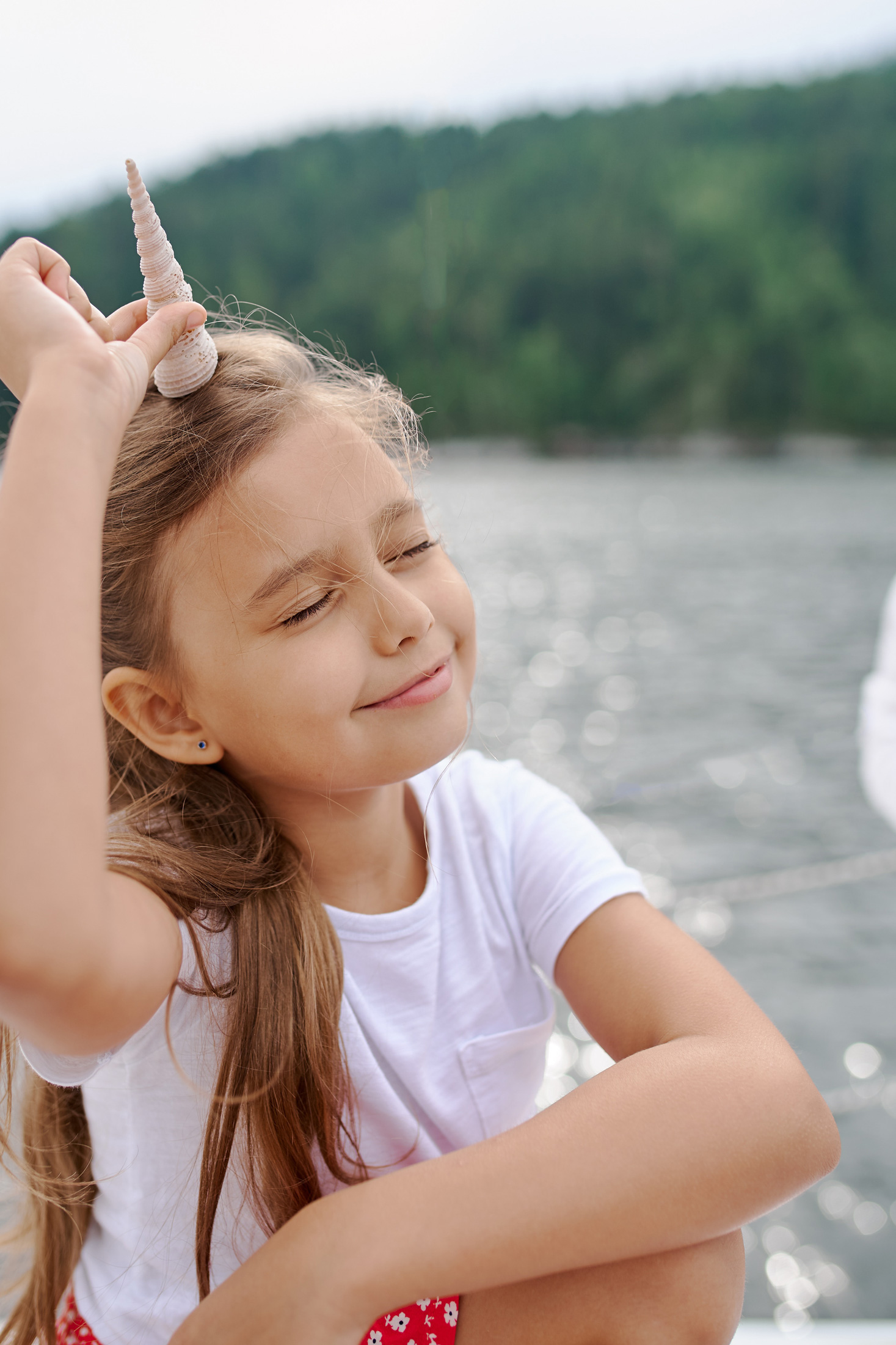 Young girl holds a shell to her forehead like a unicorn.