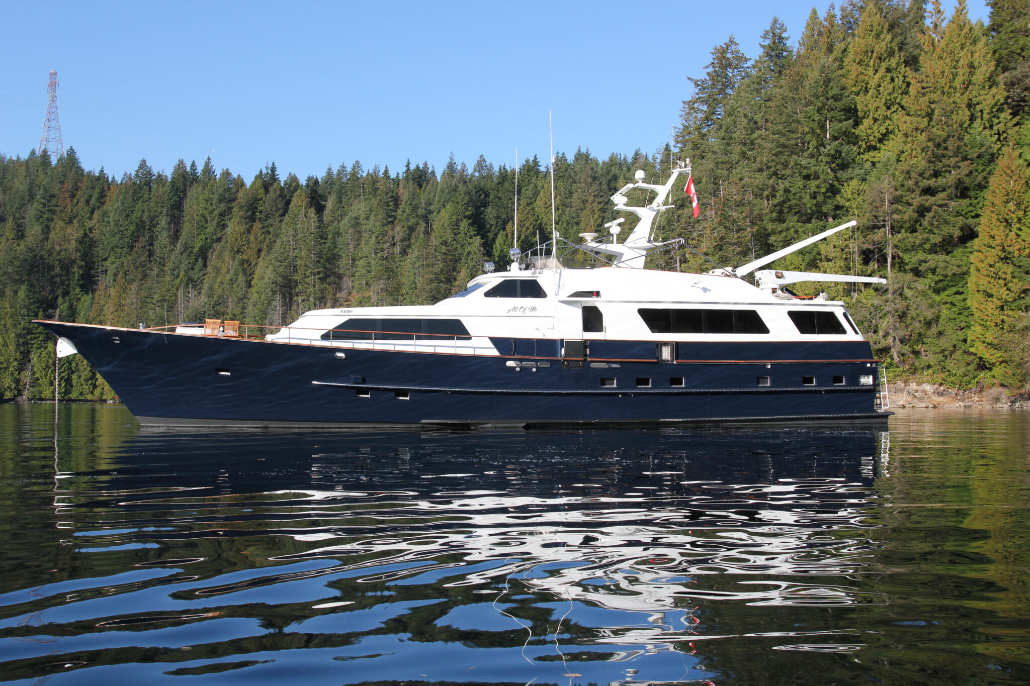 Exterior of All of Me, Vancouver's luxury superyacht. The yacht is in the foreground with a beautiful forest behind it.