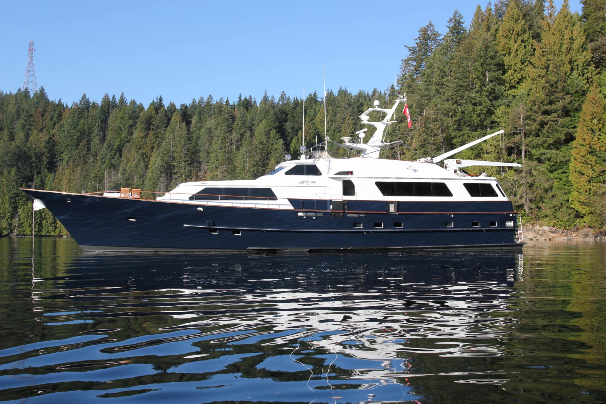 Exterior of All of Me, Vancouver's luxury superyacht. The yacht is in the foreground with a beautiful forest behind it.